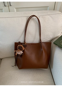 Detail of dark brown lychee textured tote bag with a cute plush bear charm on a sofa