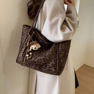 Detailed shot of large leopard print tote bag with plush bear charm on wool coat