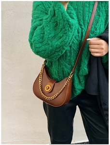 Dettaglio borsa a mezzaluna marrone con catena dorata e fibbia indossata da modella