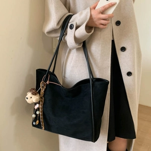 Close-up of black suede tote bag with cute bear charm and beads on long straps