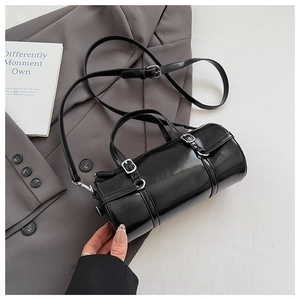 Detail of black patent leather cylinder bag with silver buckles and sleek shiny finish