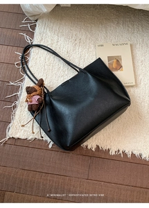 Close-up of black lychee grain leather tote bag with a cute bear plush charm