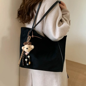 Detail of black suede tote bag featuring a cute plush bear pendant with leopard bow