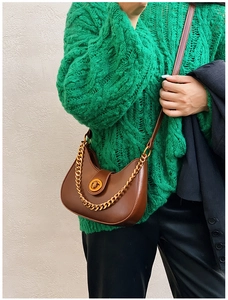 Dettaglio borsa hobo con catena dorata e fibbia indossata su un maglione verde