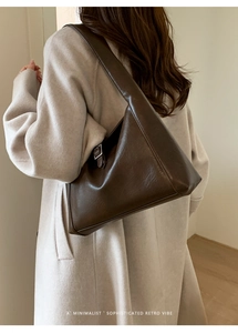 Detail of deep brown leather retro shoulder bag with silver buckle on beige coat