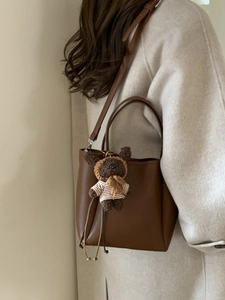 Brown lychee leather bucket bag with cute bear charm on beige coat background