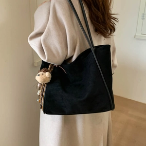 Detail of black suede tote bag with minimalist shoulder straps and cute bear pendant