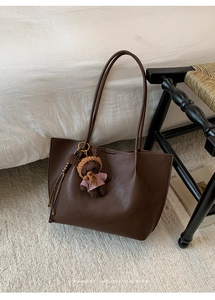 Detail view of deep brown litchi pattern leather tote bag with a cute plush bear charm