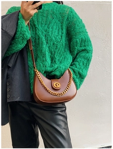 Dettaglio borsa a mezzaluna marrone con catena dorata su maglione a maglia verde