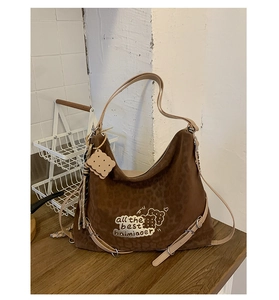 Detail of leopard print hobo bag with cartoon cookie charm and printed text on faux suede