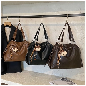 Dettaglio di tre grandi borse shopper in marrone, nero e caffè con ciondoli a forma di orso