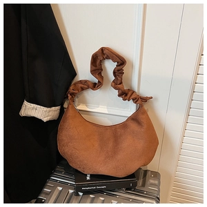 Close-up of brown suede hobo bag with pleated handle on a book in travel setting