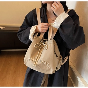 Beige canvas drawstring backpack with YOUIBEAR embroidery worn on black coat