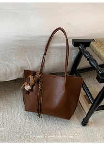 Close-up of brown pebbled leather tote bag featuring a cute knit bear charm
