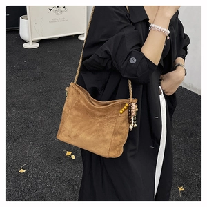 Détail d'un sac à bandoulière en daim marron avec sangle tissée et breloque perlée