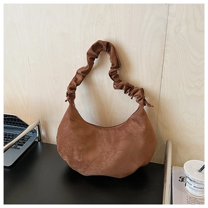 Close-up of brown suede dumpling bag with pleated drawstring strap on a wooden desk