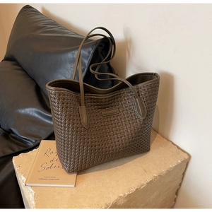 Detailed close-up of dark brown woven leather tote texture on a minimalist stone base