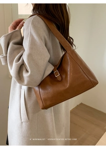 Brown leather crescent bag worn by model over a beige coat in minimalist interior