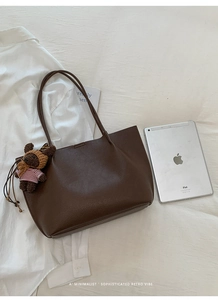 Detail of dark brown leather tote bag with a small bear charm next to an iPad for size