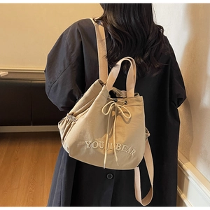 Detail of beige drawstring canvas backpack showing YOU JI BEAR embroidery and soft texture