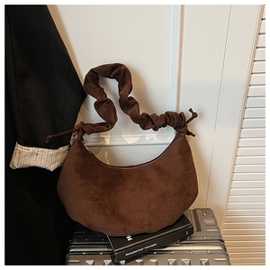 Close-up of a dark brown suede croissant bag with ruched handle on a silver suitcase