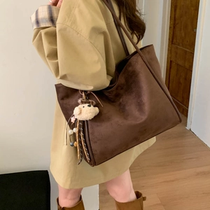 Detail of dark brown suede tote bag with plush bear charm and tassel on long shoulder strap
