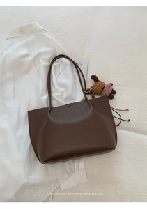 Detail of dark brown pebble texture tote bag with a cute bear charm on white shirt