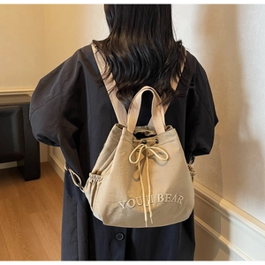 Detail of khaki nylon bucket backpack featuring drawstring closure and Youji Bear embroidery