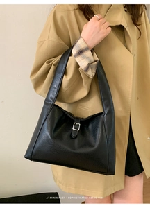 Detail of black tote bag featuring leather texture and silver buckle strap on shoulder strap