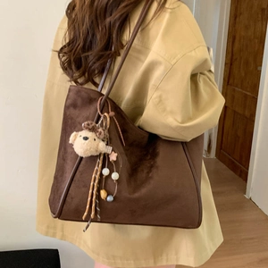 Detail view of large brown faux suede tote bag with a cute bear charm on a model