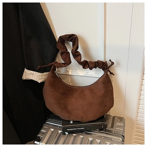 Detail of dark brown dumpling bag with ruched handle on a vintage travel suitcase