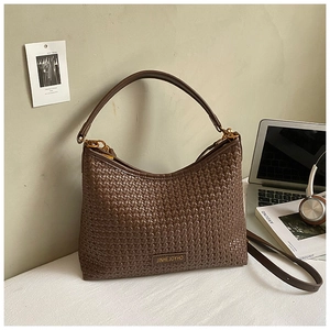 Detailed texture of dark brown woven crescent bag with adjustable strap and metal logo plate
