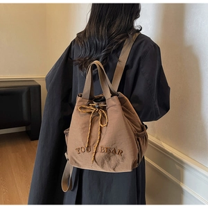 Rear view of a model wearing the brown drawstring bucket backpack with YOU BEAR embroidery