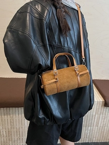 Brown suede cylinder shoulder bag with leather strap worn by model in a minimalist setting