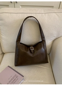 Close-up of a dark brown retro tote bag with buckle detail on a beige fabric sofa