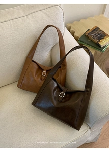 Detail view of caramel and dark brown tote bags with vintage buckle on a soft white sofa