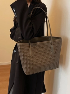 Olive grey woven tote bag with long straps worn by a woman in professional black blazer