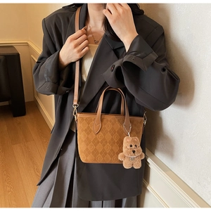 Detail view of brown suede bucket bag with quilted texture and cute bear pendant accessory