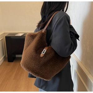 Brown faux fur tote bag with leather strap worn by model in a cozy indoor setting