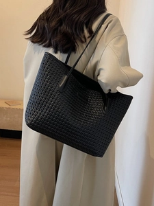 Black woven leather tote bag with long straps worn by a model in a minimalist setting