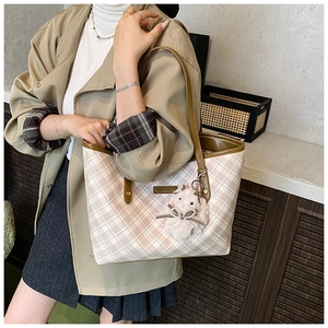 Detail view of plaid tote bag with brown leather handles and plush bunny charm accessory