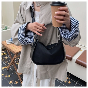 Sac bandoulière demi-lune en daim noir porté dans un décor de café extérieur automnal