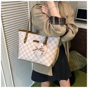 Detail of pink plaid tote bag with brown leather handles and a plush bunny charm