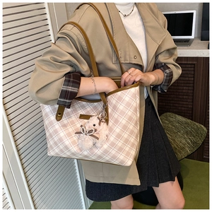 Close-up of beige plaid tote bag with brown leather strap and plush rabbit pendant