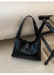 Detailed close-up of textured black leather tote bag with silver square buckle