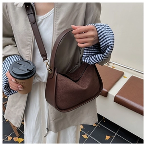 Sac hobo marron en daim avec garniture en cuir et détails dorés dans un décor d'automne