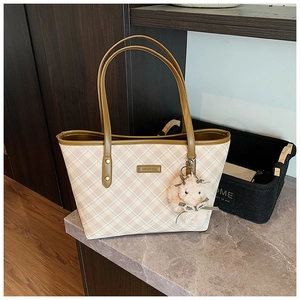 Detailed view of beige plaid tote bag featuring brown leather trim and plush bunny charm