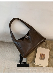 Detail of dark brown leather hobo bag with silver buckle on a woven chair