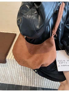 Brown suede dumpling crossbody bag with adjustable wide strap and minimalist pleated design