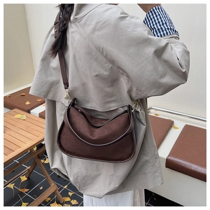 Detail of dark brown suede crossbody bag with gold hardware in autumn outdoor setting